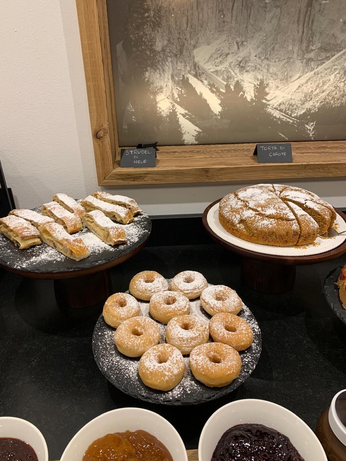 En udstilling af kager, heriblandt strudel, gulerodskage og donuts, med skilte der angiver navnene.