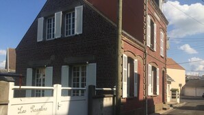 En toetages murbygning med hvide skodder, en portindgang og en garage i baggrunden.