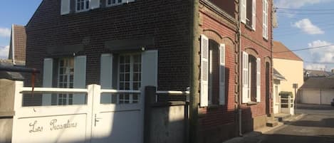 Um edifício de dois andares em tijolo com portadas brancas, uma entrada com portão e uma garagem ao fundo.