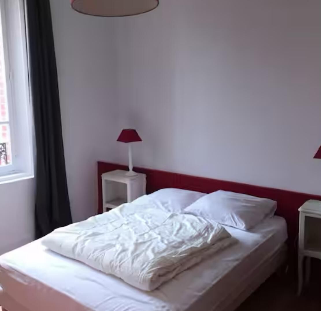 A neatly made bed with white bedding, a red headboard, and two bedside tables with lamps.