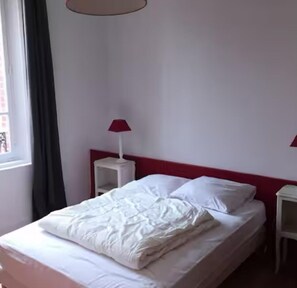 A neatly made bed with white bedding, a red headboard, and two bedside tables with lamps.