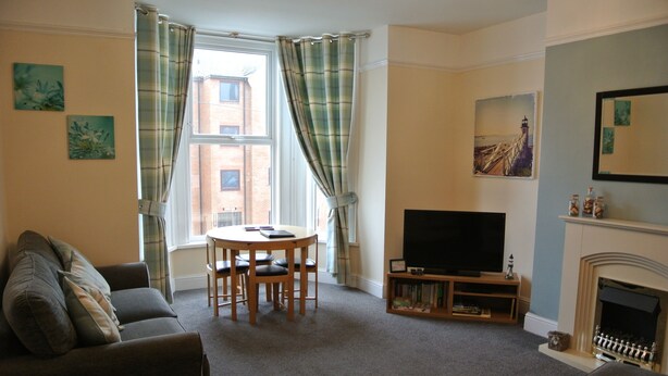 A living room with a sofa, a round table with chairs, a television, a fireplace, and a window with curtains.