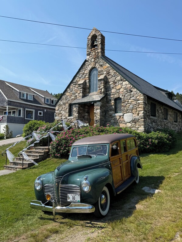 A vintage green car parked in front of a stone church with a bell tower.