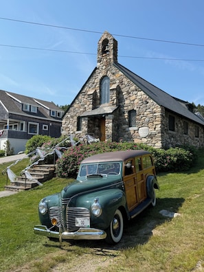 A vintage green car parked in front of a stone church with a bell tower.