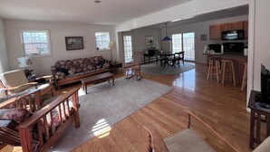 A spacious living room with a sofa, a dining table, and a kitchen area with wooden cabinets and a microwave. - Welcome to Owl House - Your Coastal Retreat in East Boothbay! (Boothbay)
