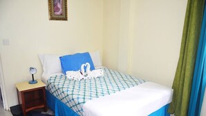 A neatly made bed with a checkered bedspread, a white comforter, and two pillows. There is a small bedside table with a lamp and a framed picture on the wall above the bed. - Louislyn Apartments #8 Quiet and Scenic (Picard)