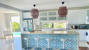 Een moderne keuken met witte kasten, een blauwe tegelwand en een groot kookeiland met barstoelen.