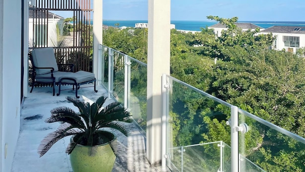 Een balkon met een stoel, een grote potplant en uitzicht op zee en groen.