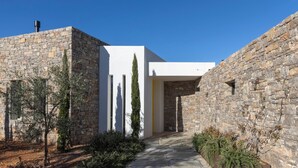 A stone building with a modern white structure, a stone pathway, and evergreen shrubs.