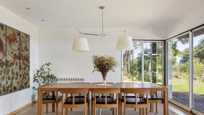A dining area with a wooden table and chairs, a vase with dried flowers, and a large window with a view of greenery. - SeaView Oasis: 4BR, Pool, Tennis by Host For Us (Alcabideche)