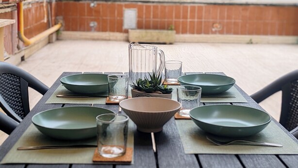A table set with green bowls, glasses, and a pitcher, surrounded by chairs, in an outdoor patio area. - Family apartment near the Vatican. Well connected. 2 terraces. WIFI. (Roma)