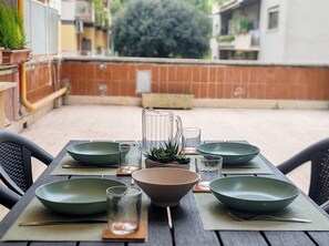A table set with green bowls, glasses, and a pitcher, surrounded by chairs, in an outdoor patio area.