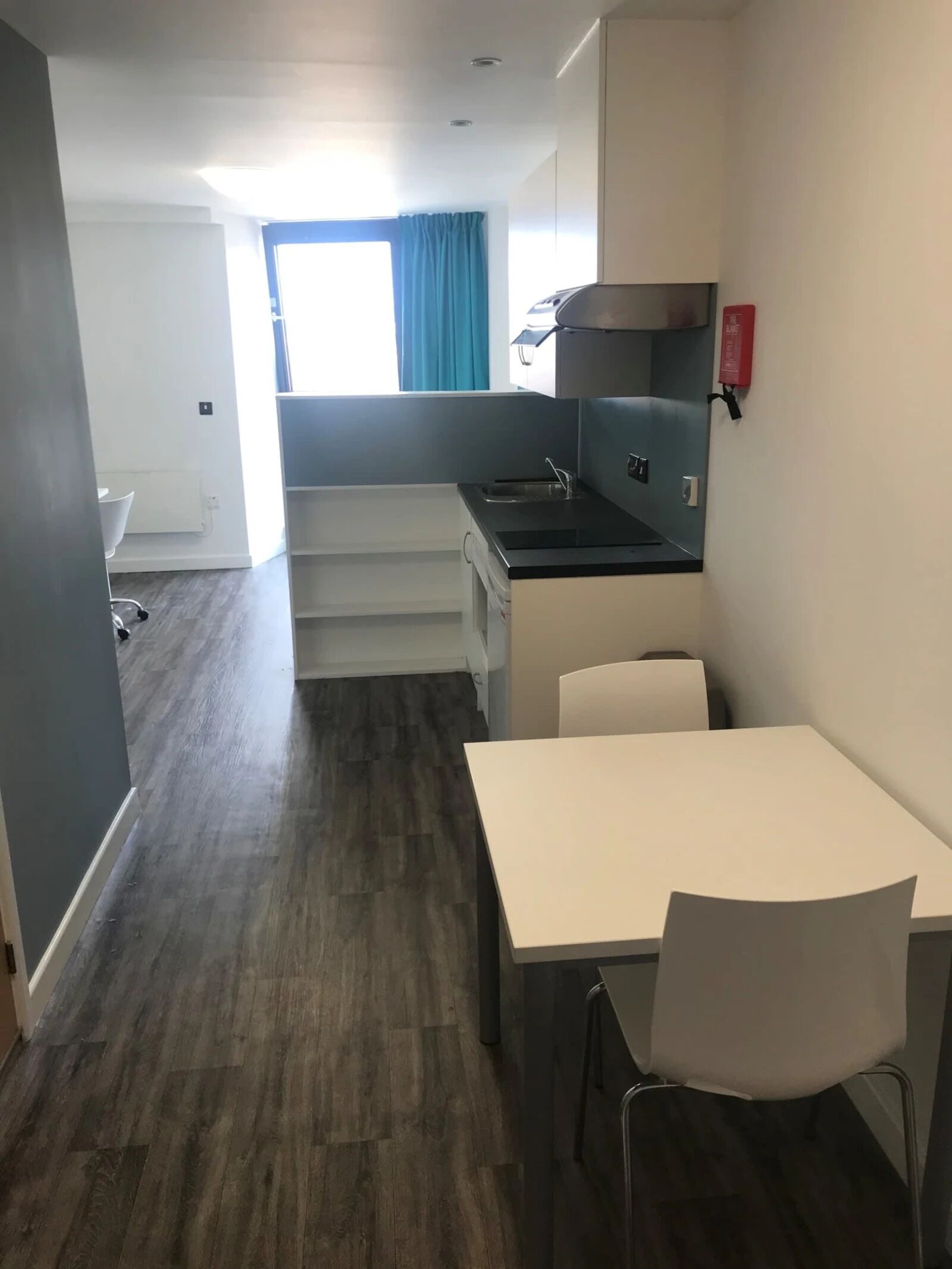 Een compacte keuken met een spoelbak, kookplaat en een klein eethoekje met een tafel en stoelen.