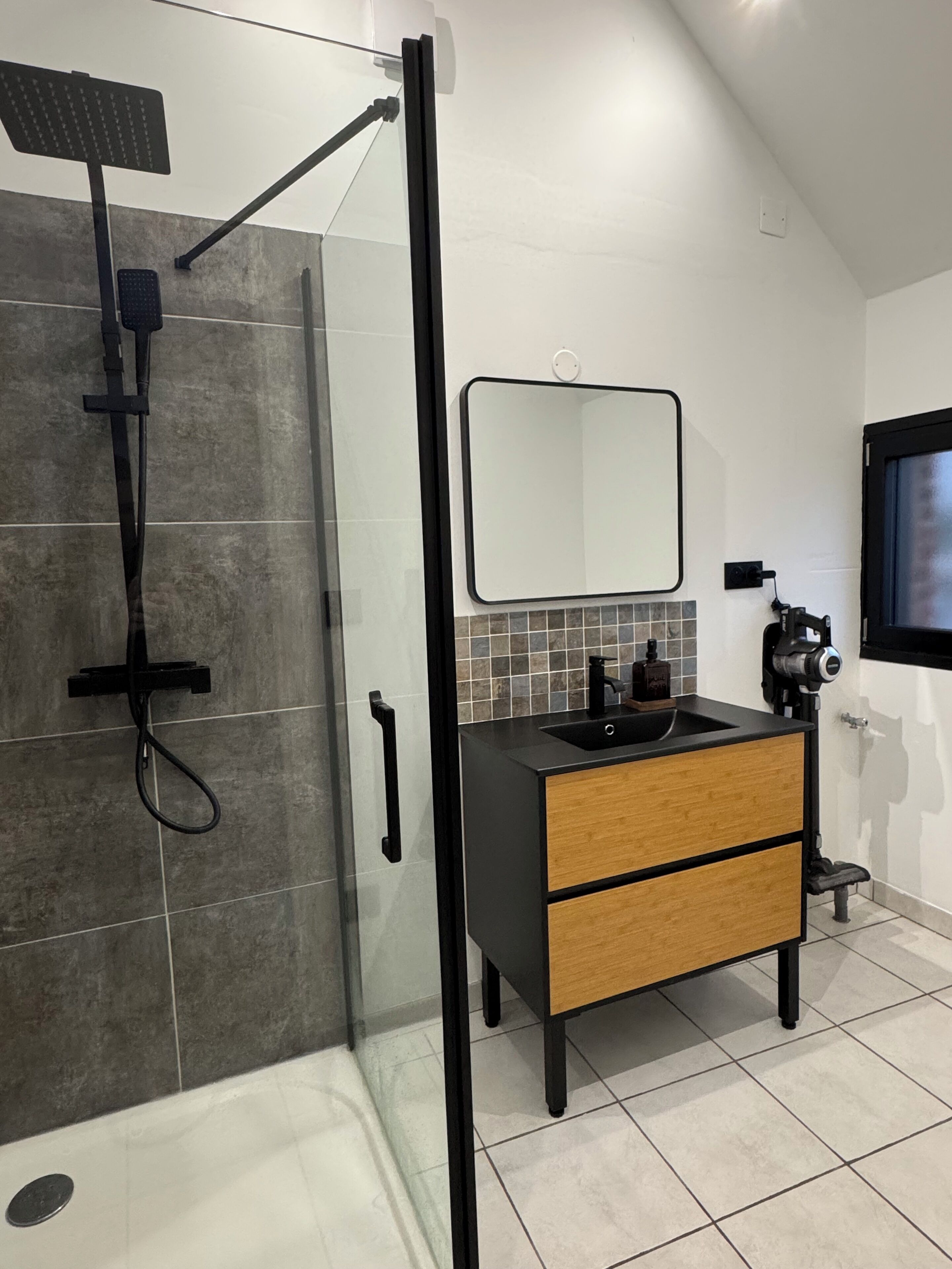 Een moderne badkamer met een douchecabine van glas, een zwart wastafelmeubel met een houten onderkast en een spiegel boven de wastafel.