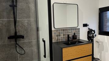 Een moderne badkamer met een douchecabine van glas, een zwart wastafelmeubel met een houten onderkast en een spiegel boven de wastafel.