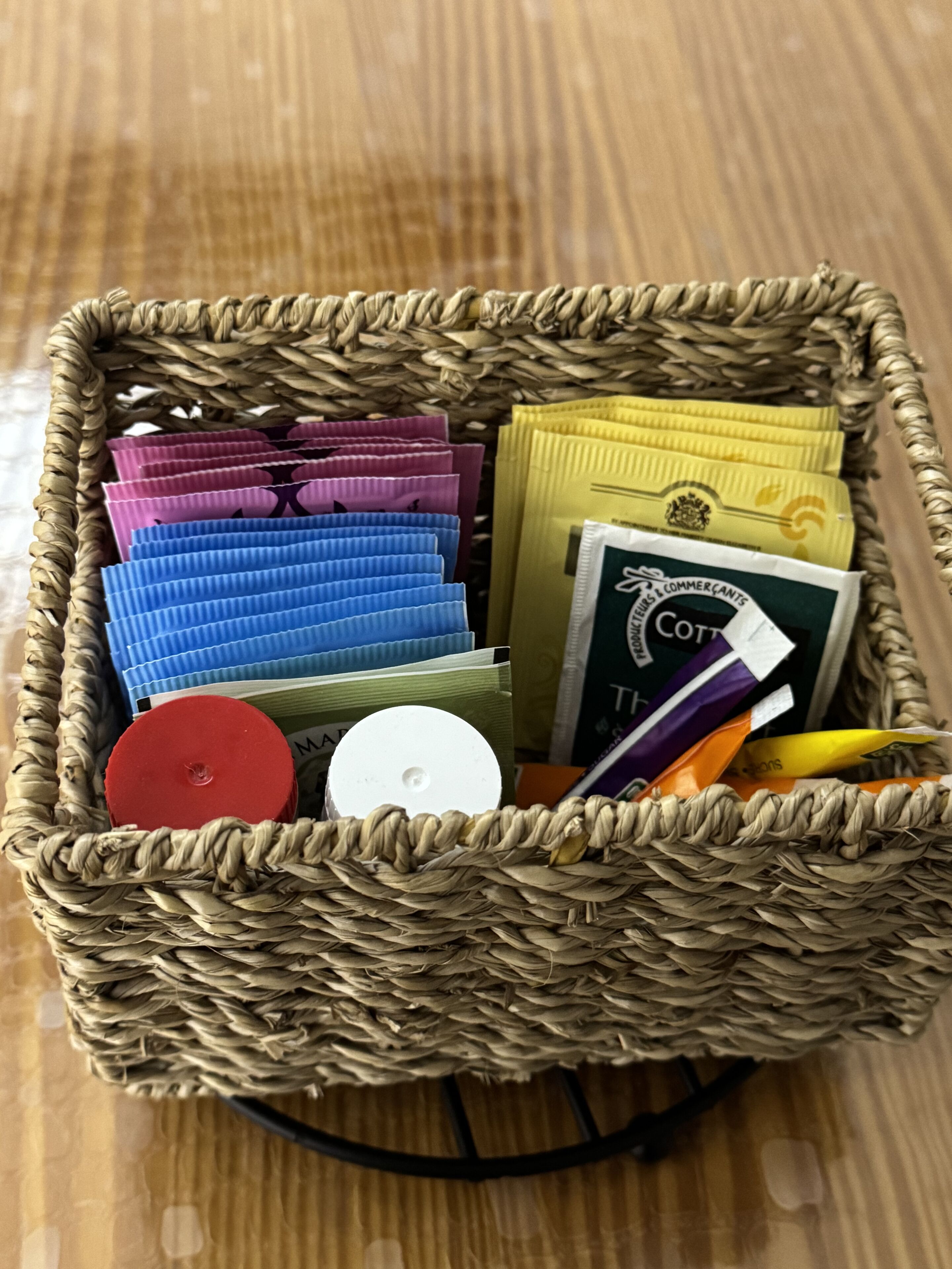 A wicker basket containing various items including colorful packets, a white circular object, and a book with a green cover.