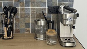 Une cuisine équipée d’une machine à café, d’une bouilloire et d’un moulin à café, le tout posé sur le plan de travail.