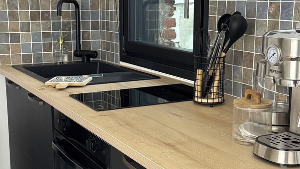 Une cuisine moderne avec un évier noir, un plan de travail en bois et une cuisinière intégrée.