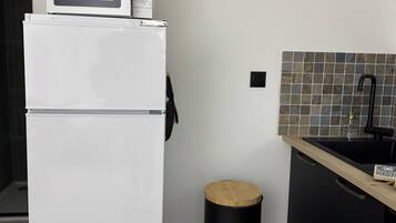 A compact kitchen with a white refrigerator, a microwave, a black trash bin, and a black sink with a tiled backsplash.