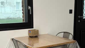 Une table à manger avec un plateau en bois et des chaises en métal, recouverte d’une nappe en plastique transparent.