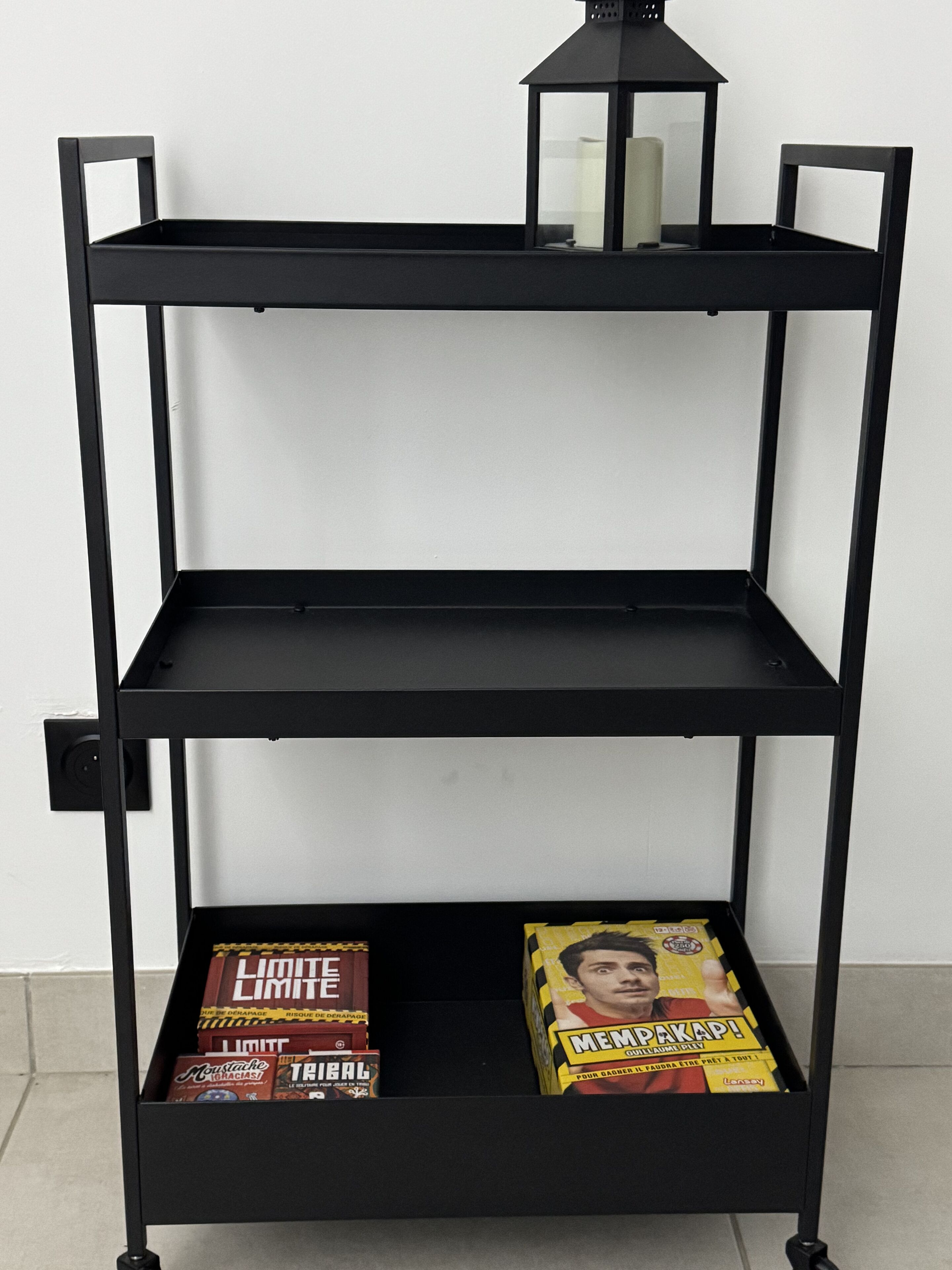 Une étagère en métal noir avec deux tiroirs, dont l’un contient des magazines et l’autre des livres.