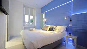 Un dormitorio moderno con una cama grande, una mesita de noche pequeña y una ventana con persianas.