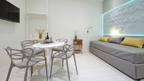 Una sala de estar moderna con un sofá gris, una mesa de comedor blanca con cuatro sillas y un televisor de pantalla plana montado en la pared.