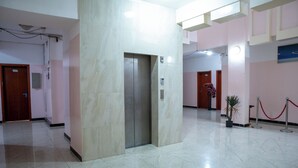 Een ruime lobby met een marmeren vloer, een centrale lift en een rode lintbarrière.