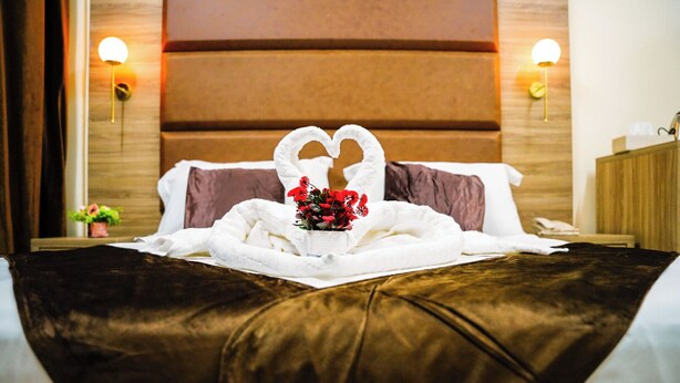 Een hotelkamer met een bed, voorzien van een handdoekje gevouwen in de vorm van een hart en een boeket rode bloemen.