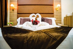 A hotel room with a bed featuring a heart-shaped towel arrangement and a bouquet of red flowers. - COMFORT HOTEL (Djibouti)