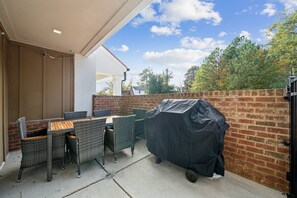 Eine Terrasse im Freien mit einem überdachten Grill, Korbmöbeln und einer Backsteinmauer.