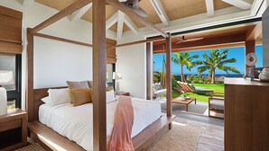Un dormitorio espacioso con una cama grande, vigas de techo de madera y vistas al océano y palmeras.