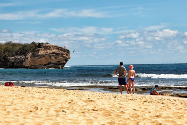 A sandy beach with a rocky cliff and ocean waves.