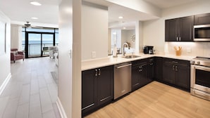 A modern kitchen with dark cabinets, stainless steel appliances, and a large window overlooking the sea. - Welcome to Captain's Bridge with two Ocean Front Primary Suites (Myrtle Beach)