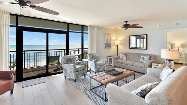 A spacious living room with a balcony overlooking the sea, furnished with a sofa, armchairs, and a coffee table. - Welcome to Captain's Bridge with two Ocean Front Primary Suites (Myrtle Beach)
