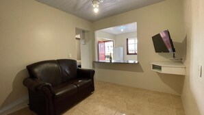 Een woonkamer met een donkerbruine leren bank, een flatscreen-televisie aan de muur en een klein wit schap.