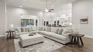 A modern living room with a sectional sofa, a coffee table, and a dining area with chairs. - This beautiful 3200 SF single storey with loft backs onto a heavily treed forest (Dallas)
