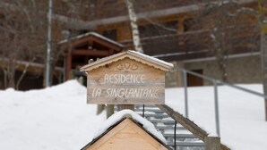 Ein hölzernes Schild mit der Aufschrift 'RESIDENCE LA SINGLANTANE' vor einem Gebäude mit geneigtem Dach.