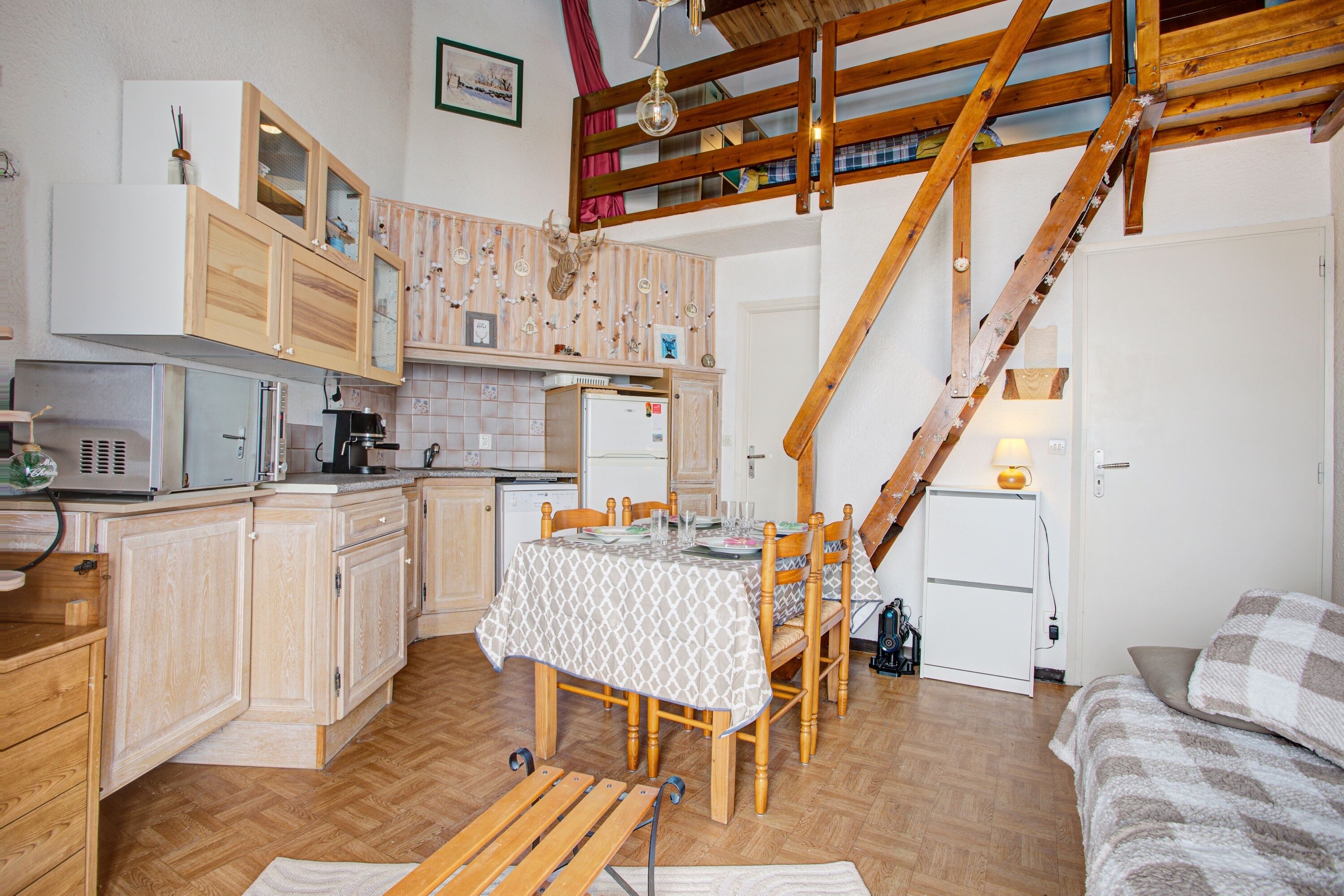 A compact kitchen with wooden cabinets, a dining table, and a staircase leading to an upper level.