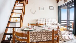 Ein Essbereich mit einem Holztisch, gedeckt für vier Personen, einem Holzstuhl, einer Leiter und einem Bett mit karierter Bettdecke.