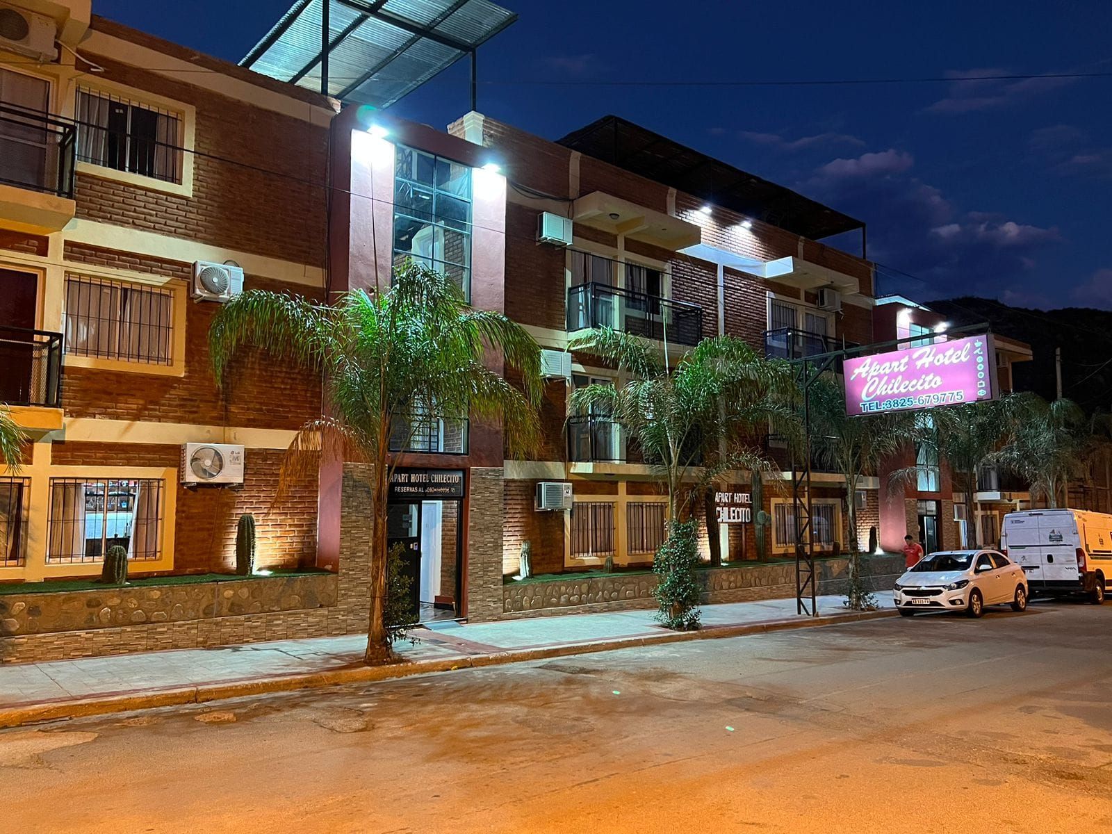 A multi-story hotel with balconies, a signboard, and a parked van.