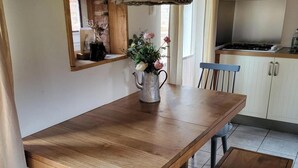 Une table à manger en bois avec des bancs, un luminaire suspendu, un coin cuisine avec des placards et un miroir au mur.