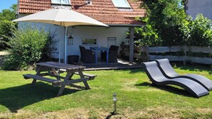 Une maison avec un toit recouvert de tuiles rouges, une terrasse avec une table et des chaises, et un transat.