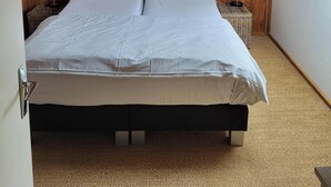 Une chambre avec un plafond en pente, un lit recouvert d’une couette à carreaux, deux tables de chevet avec des lampes et une décoration murale.