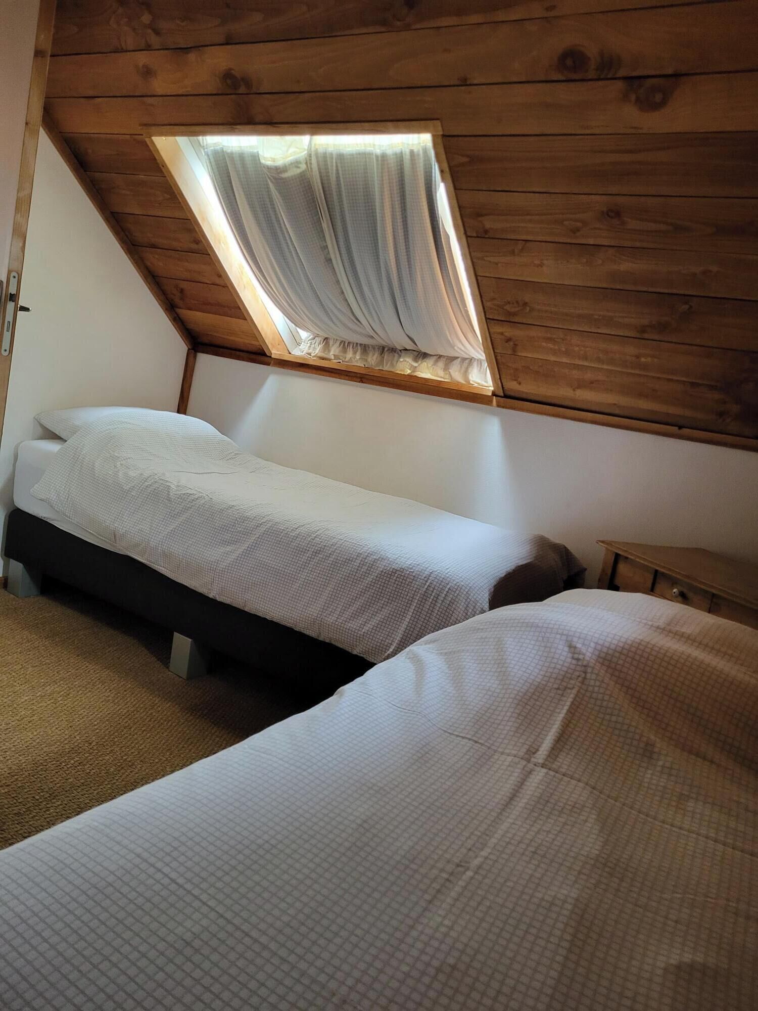 Un dormitorio con dos camas, techo de madera y una ventana con cortinas.