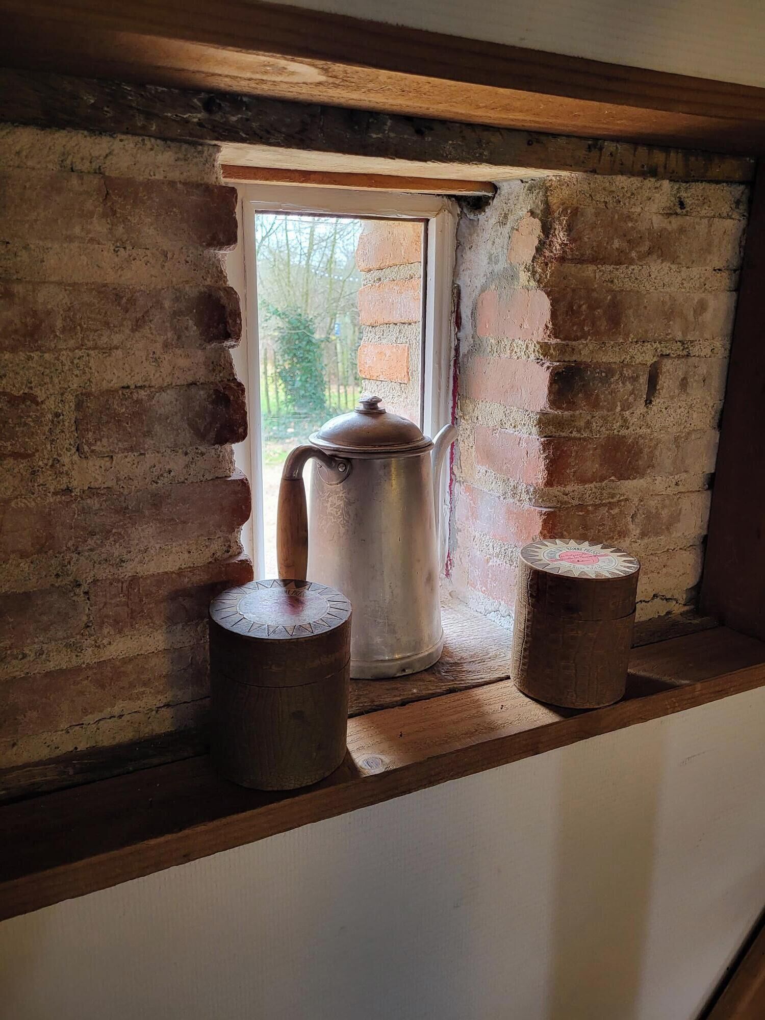 Una habitación rústica con un alféizar de madera, una olla de metal y dos recipientes de madera.
