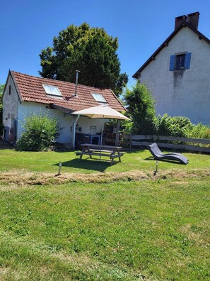 Ein Haus mit rotem Ziegeldach, einer überdachten Terrasse mit Tisch und Stühlen sowie einem grünen Rasen.