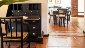 Un comedor con un escritorio negro y sillas, un espejo y cuadros en la pared.