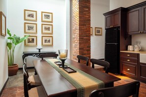 Un espace repas avec une longue table en bois, des chaises, un centre de table composé de bougies, des tableaux encadrés au mur et une cheminée en briques.