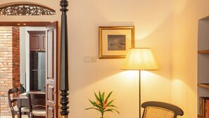 Un dormitorio con cama con dosel, una silla, una mesita con lámpara y una estantería.